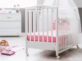 Lettino prima infanzia bianco della linea Hello di Italbaby su ruote piroettanti con cassetto sotto rete a doghe e con kit tessile disponibile rosa o azzurro